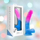 The Avant Chasing Sunsets Dildo - Mermaid by Avant, in pink and blue, stands beside its packaging displaying icons for platinum-cured silicone and a sturdy suction cup base, set against a softly blurred background.